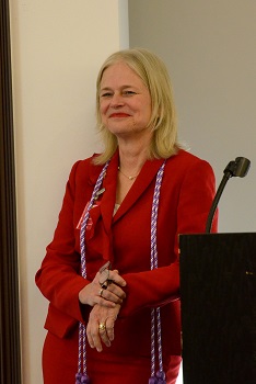 Portrait of a blonde woman wearing a red suit leaning on a podium